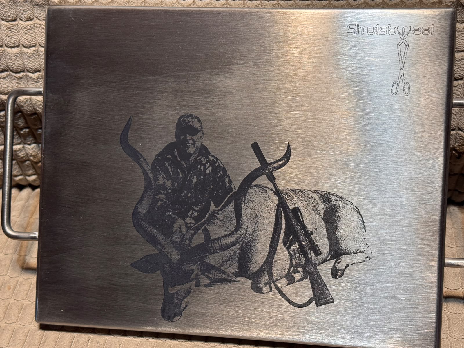 A stainless braai tray laser-engraved with a hunter kneeling beside a kudu bull