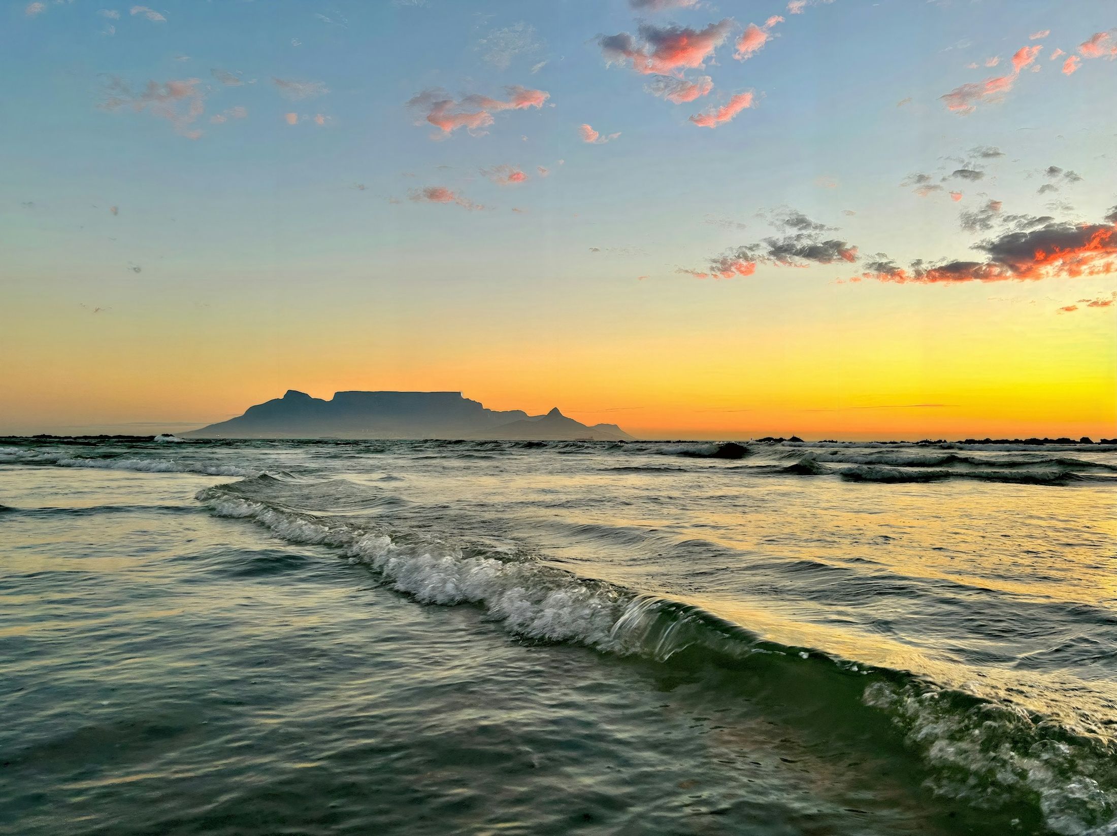 Table Mountain in silhouette across the ocean at sunset, seen from Bloubergstrand